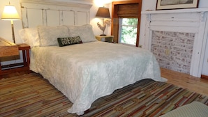 A bedroom with a large bed, two bedside lamps, a wooden nightstand, a patterned rug, and a fireplace with a brick wall. - Vogelsang guesthouse, 5 minute walk to downtown West Jefferson. (West Jefferson)