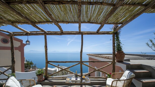 Une terrasse meublée de mobilier en osier, une table avec des boissons et une vue sur la mer.