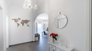 Ein moderner Flur mit Weltkarte an der Wand, einer Chandelieber, einem runden Spiegel und einer Vase mit roten Blumen.