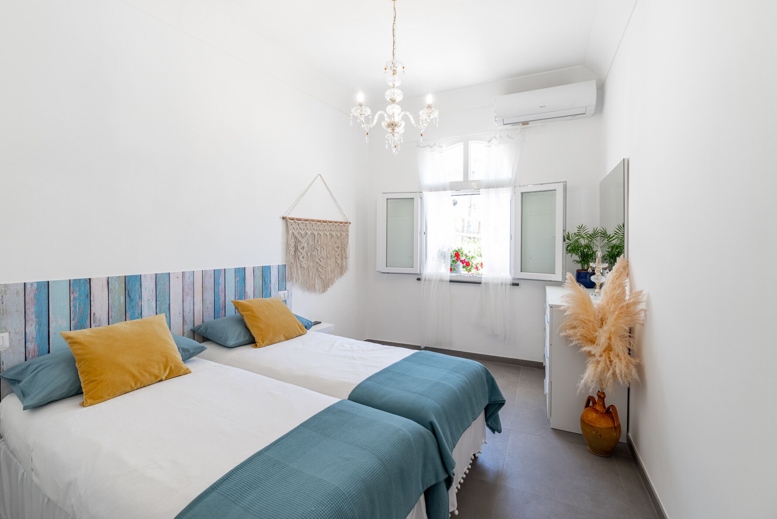 Una camera da letto con due letti, un lampadario, una finestra con tende e una pianta.