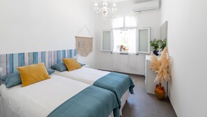 Ein Schlafzimmer mit zwei Betten, einer Chandelierleuchtre, einem Fenster mit Vorhängen und einer Pflanze.