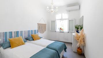 Una camera da letto con due letti, un lampadario, una finestra con tende e una pianta.