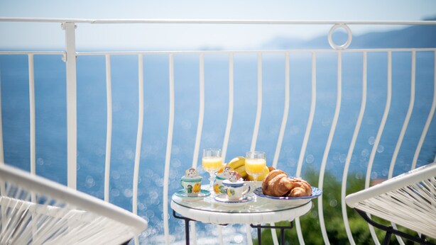 Ein Balkon mit einem für das Frühstück gedeckten Tisch, darunter Croissants, Saft und ein Teekessel.
