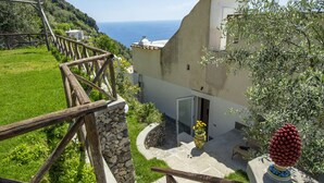A stone staircase leading to a building with a view of the sea, a wooden fence, and a potted plant. - Punta di Diamante - 200 Steps to Heaven (Praiano)