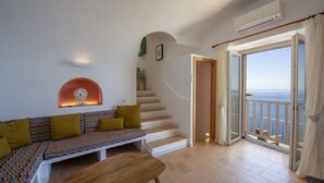 A living room with a sofa, a wooden table, a staircase, and a balcony with a view. - Punta di Diamante - 200 Steps to Heaven (Praiano)