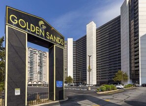 Un edificio grande con un letrero que dice 'GOLDEN SANDS' y un estacionamiento al frente.