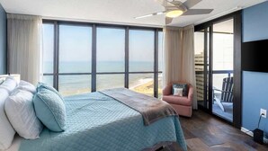 Une chambre avec un lit, une chaise, un ventilateur de plafond et une vue sur l’océan.