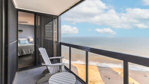 Un balcon avec vue sur l’océan, un lit avec un oreiller bleu et une chaise à rayures.