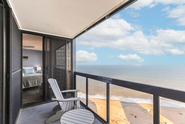 Un balcón con vista al océano, una cama con un cojín azul y una silla a rayas.