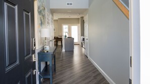 A hallway with a dark door, a blue bench, and a kitchen area in the background.