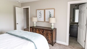 A bedroom with a bed, a dresser, two wall-mounted lamps, and framed artwork.