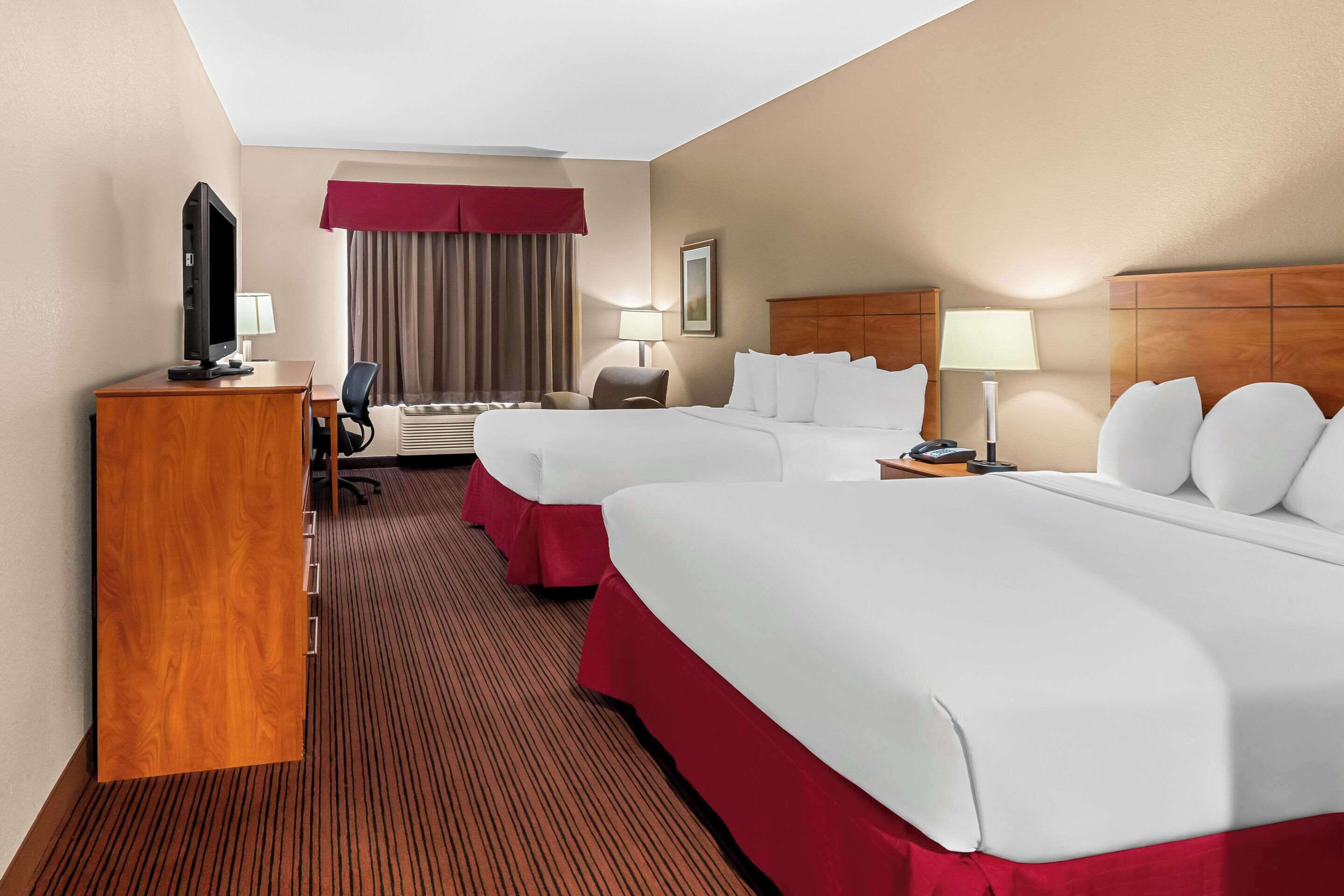 A hotel room with two beds, a desk with a television, a chair, and a lamp.