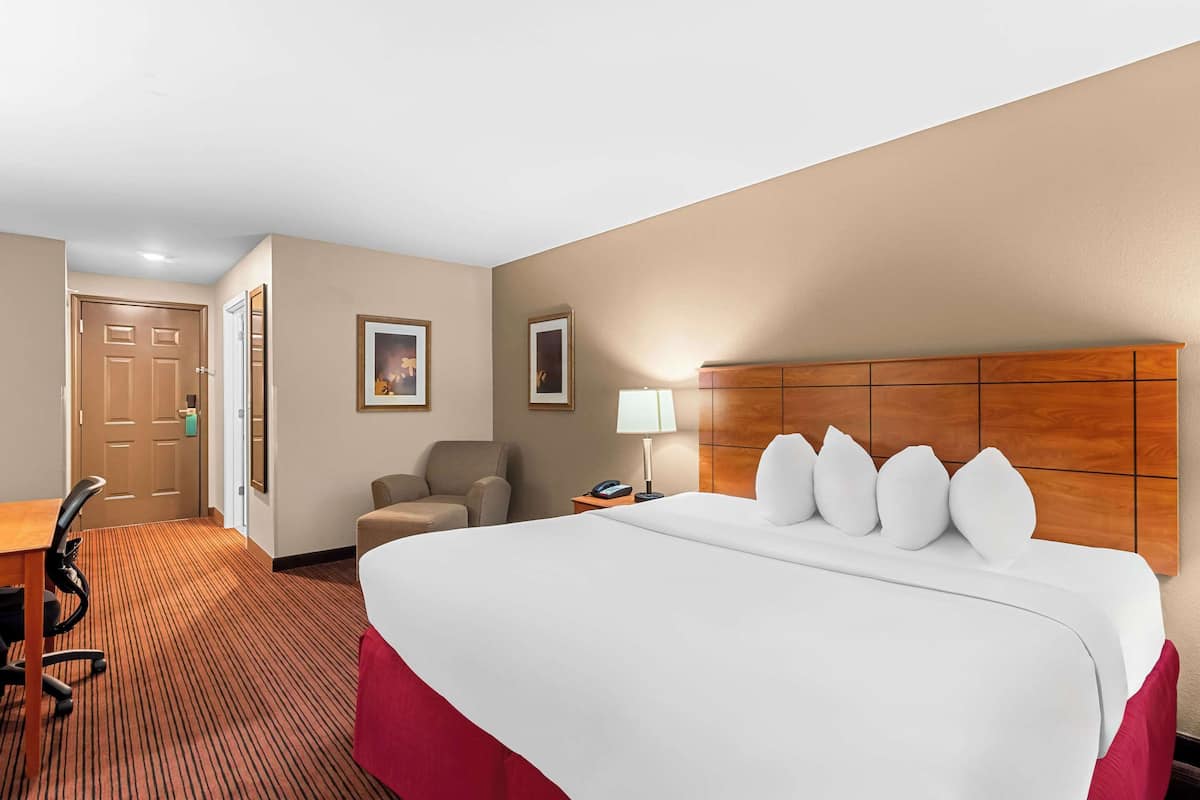 Quarto de hotel com uma cama grande, uma escrivaninha, uma cadeira e uma mesa de cabeceira com abajur.