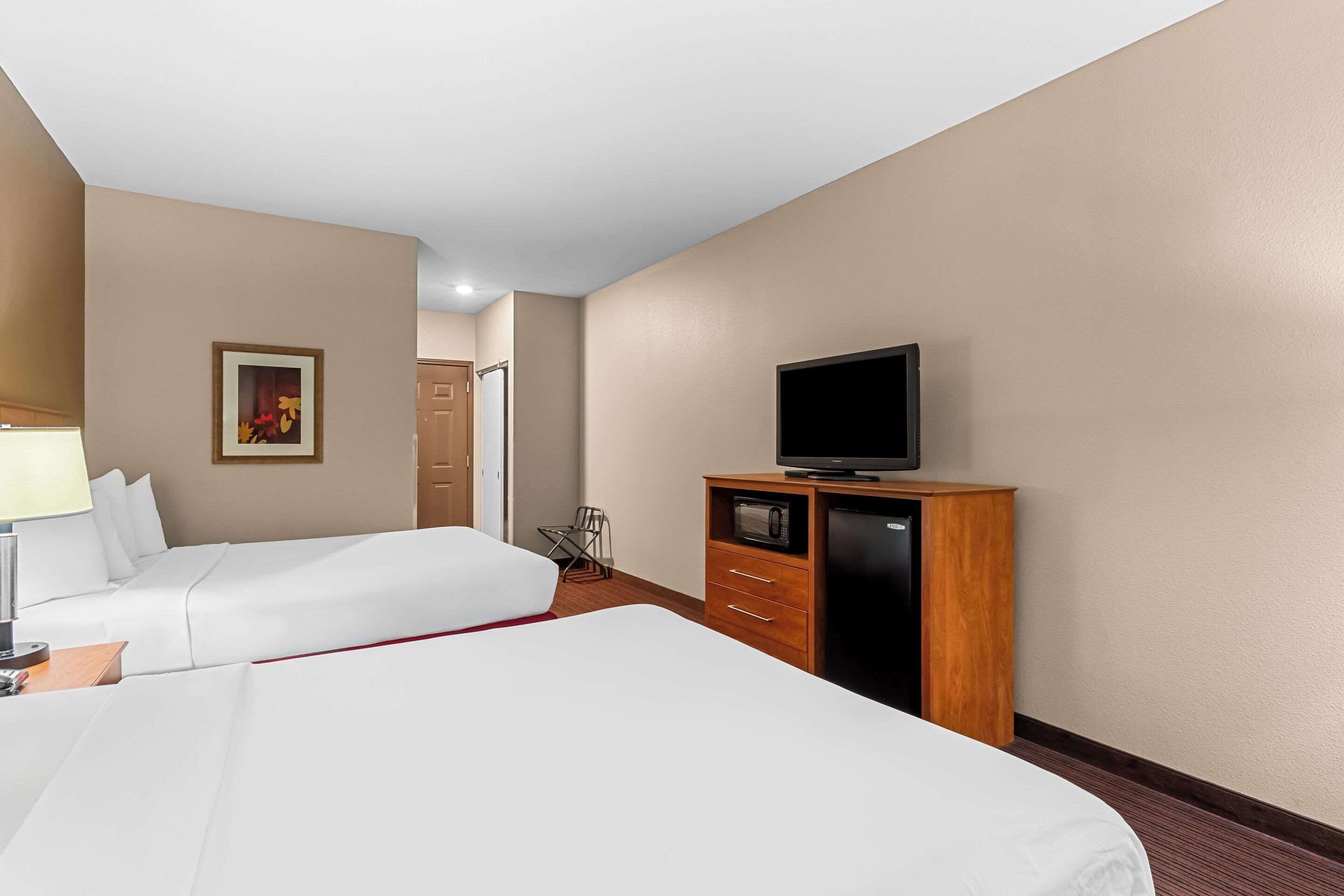 A hotel room with two beds, a television on a wooden cabinet, and a painting on the wall.