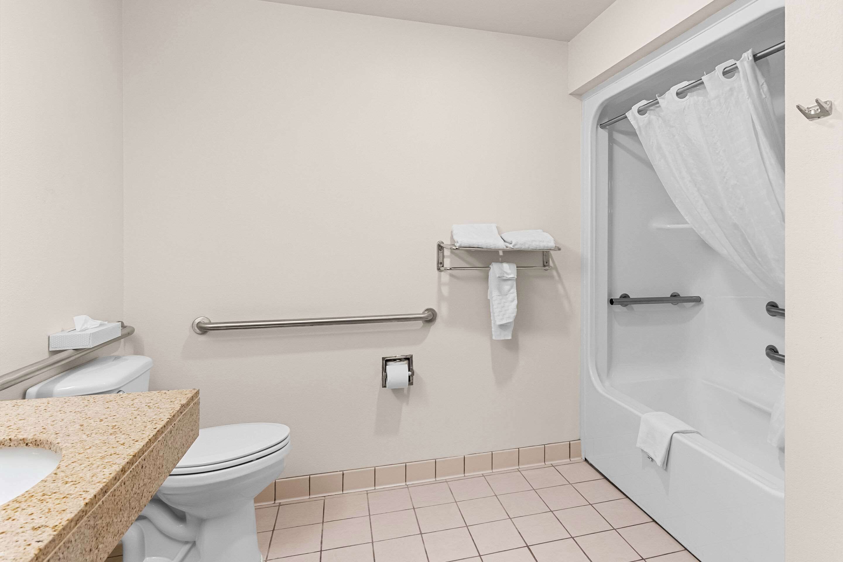 A bathroom with a toilet, sink, shower, and grab bars.