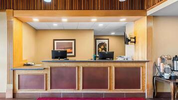 A reception area with a wooden reception desk, two computer monitors, framed pictures on the wall, and a red carpet.