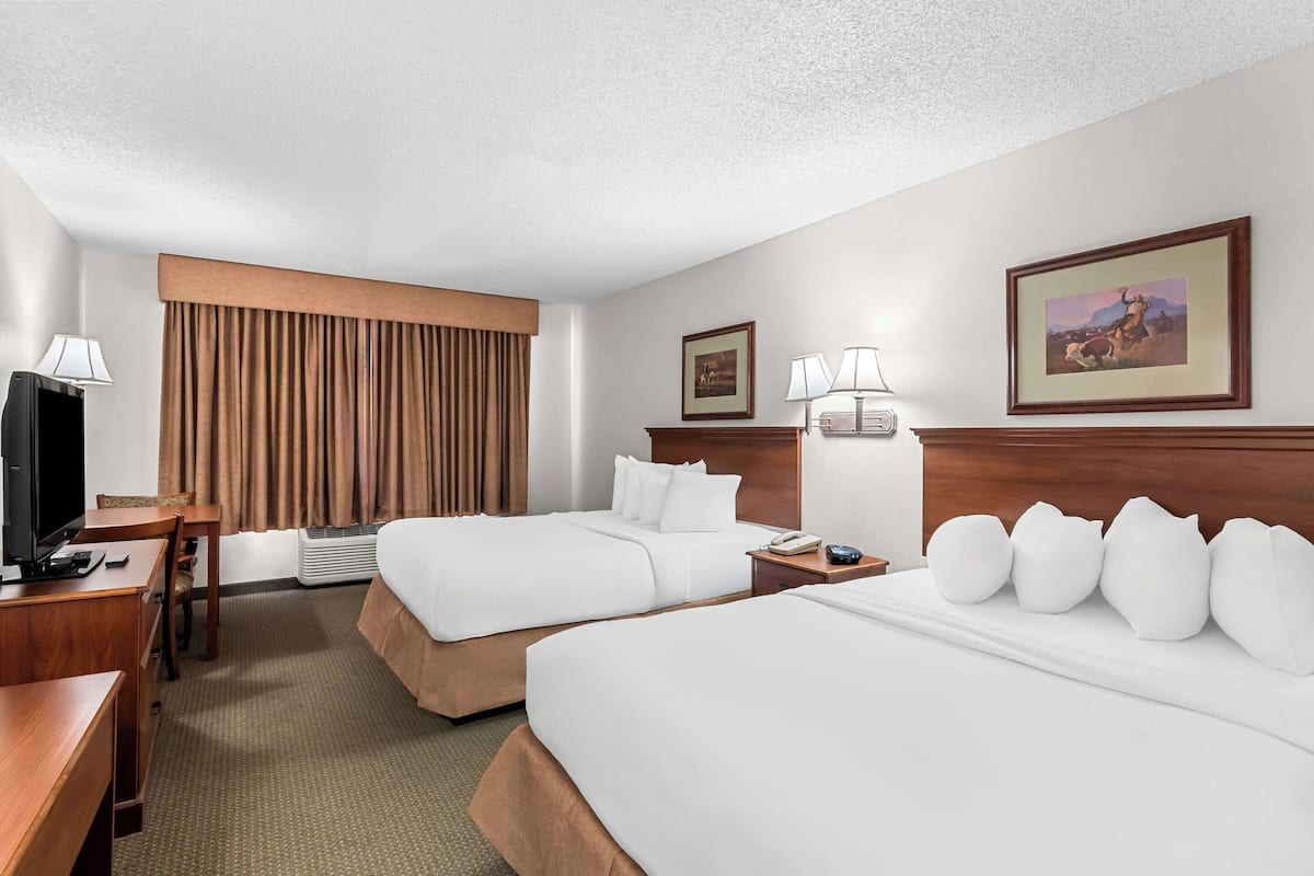 Quarto de hotel com duas camas, uma escrivaninha, televisão e uma janela grande com cortinas.