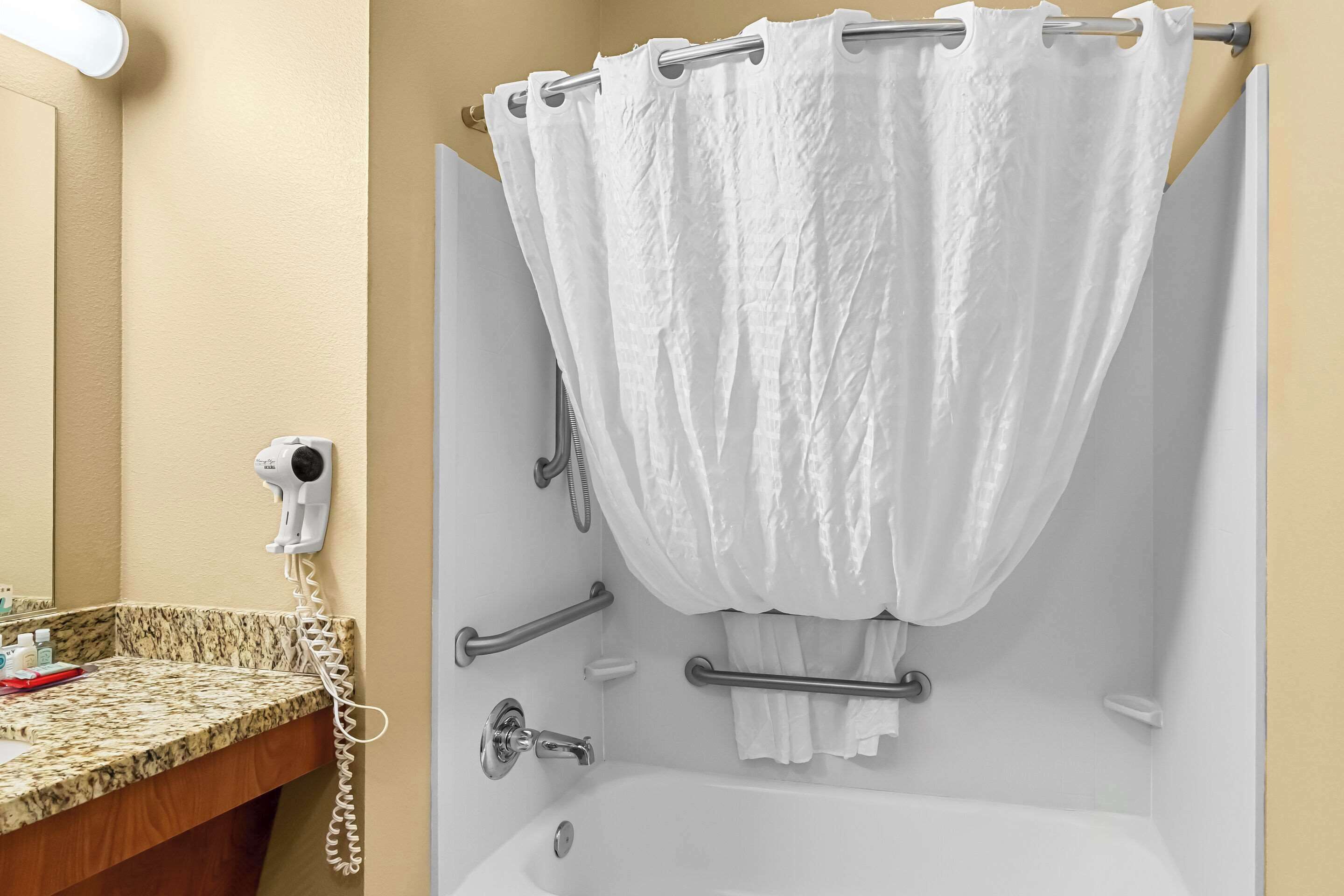 A bathroom with a white bathtub, a hairdryer, and a towel rack.