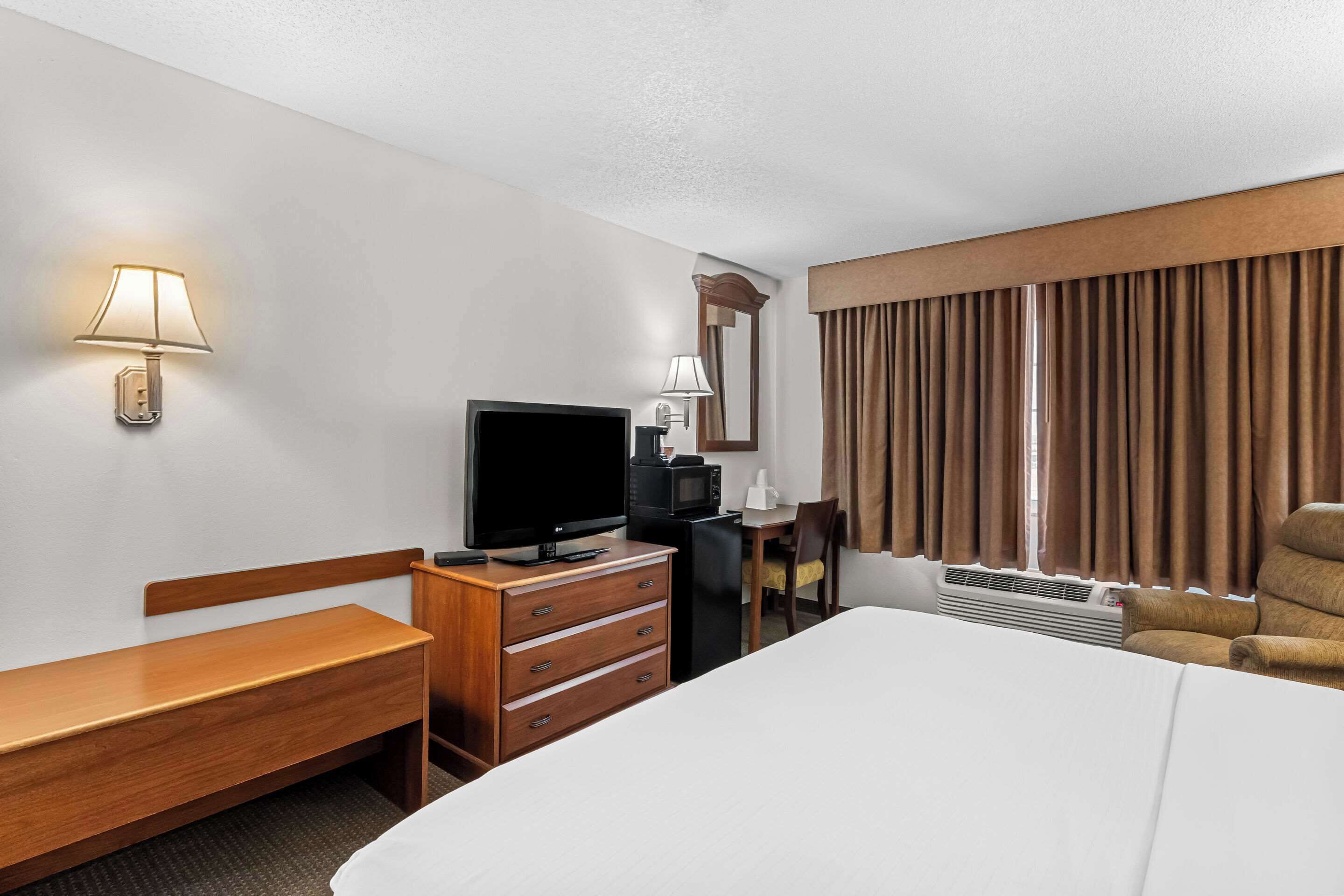 A hotel room with a bed, a desk, a television, a dresser, a chair, and a window with curtains.