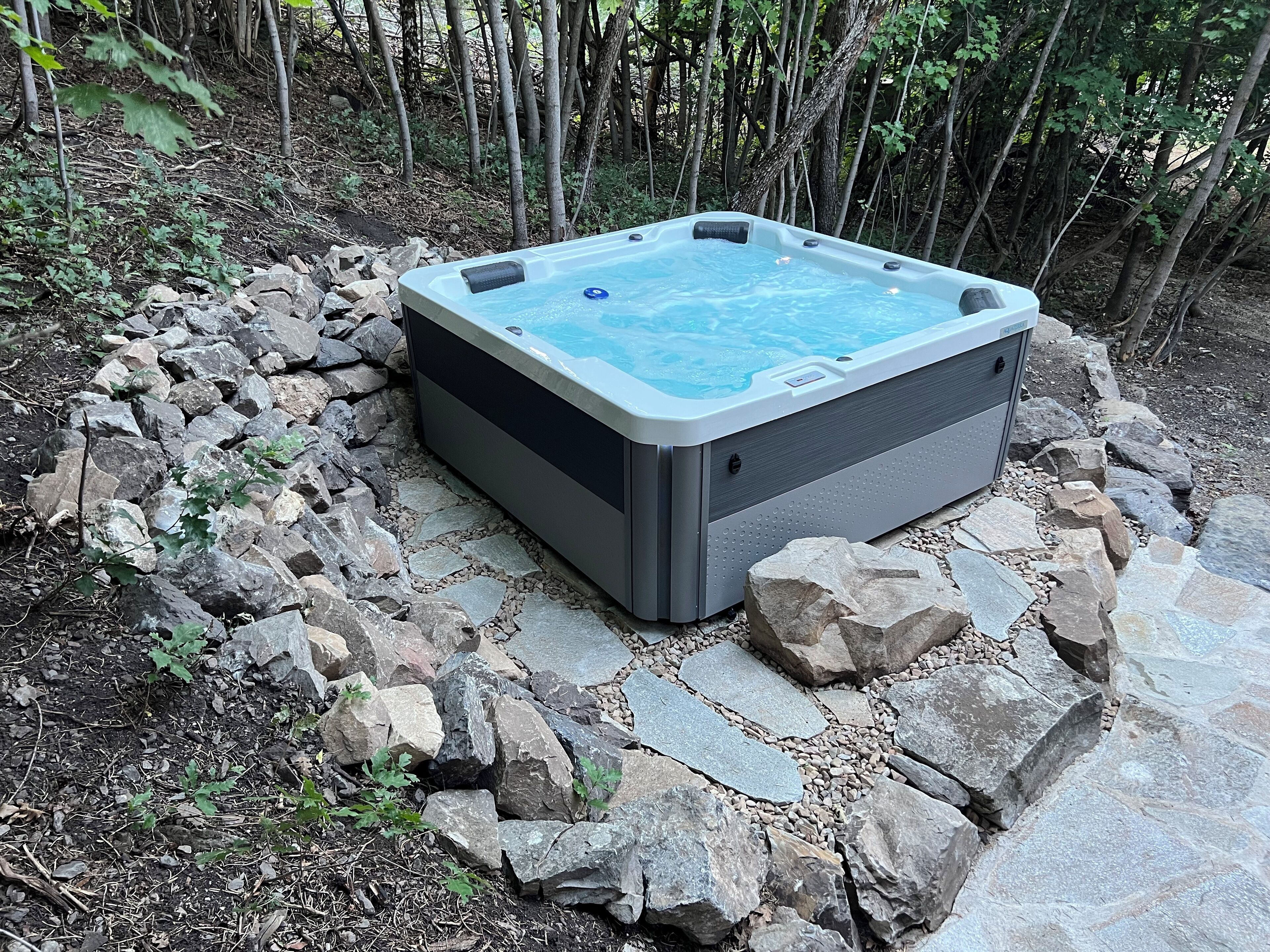 A hot tub surrounded by rocks and foliage.