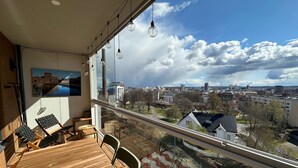 Ein Balkon mit Holztisch und -stühlen, einem Gemälde und Blick auf die Stadt.