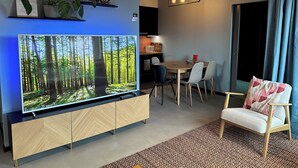 Ein modernes Wohnzimmer mit einem großen Flachbildfernseher, einem Essbereich mit Tisch und Stühlen sowie einer gemütlichen Sitzecke mit einem gemusterten Teppich.