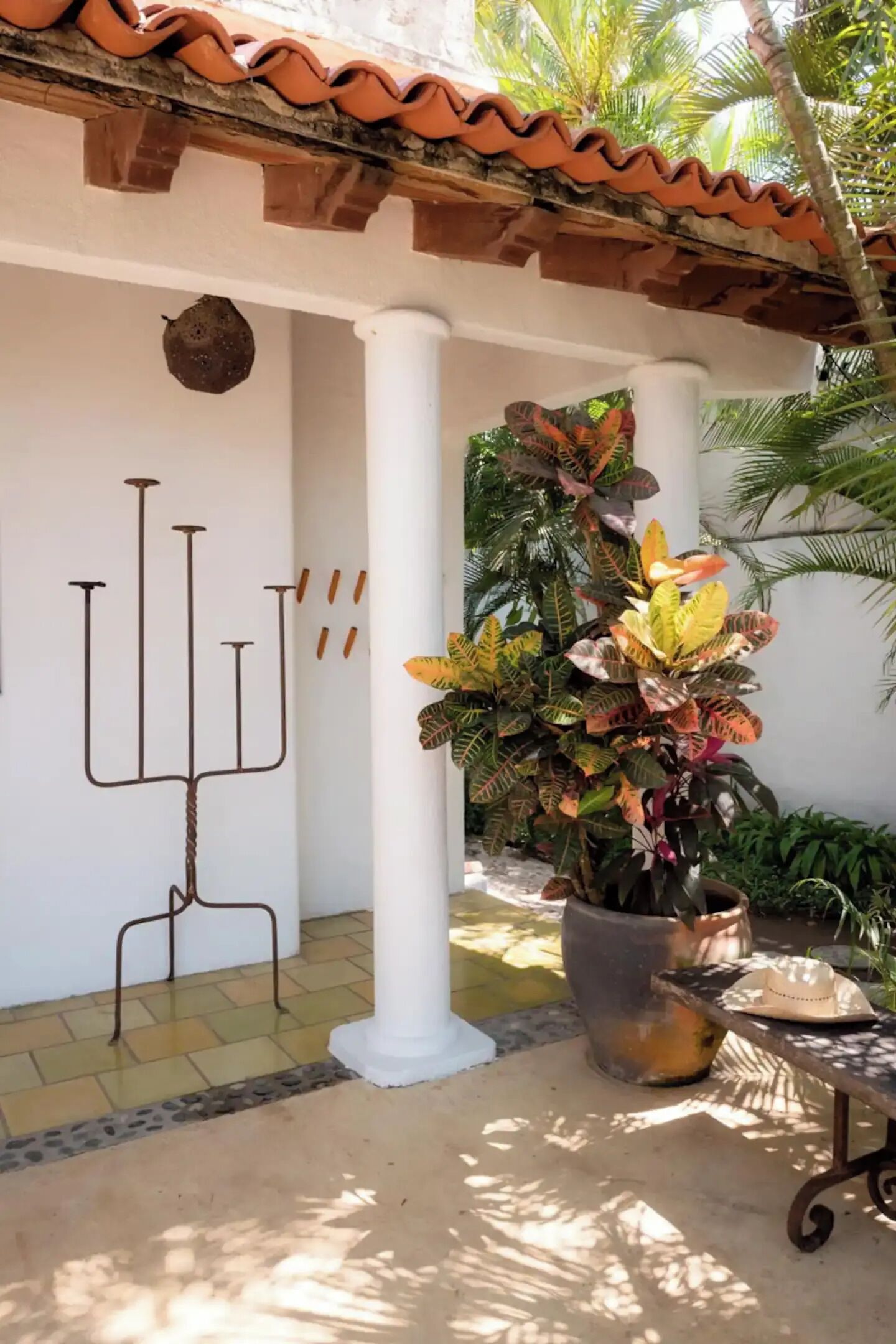 A covered outdoor area with a candelabra, a potted plant, and a table with a hat.