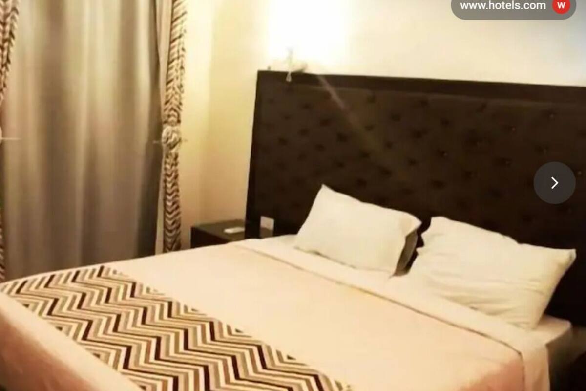 Una habitación de hotel con una cama, una mesita de noche y cortinas.