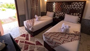 Hotelkamer met twee bedden, een gestreept hoofdeinde, een rood-wit kleed en uitzicht op groen.