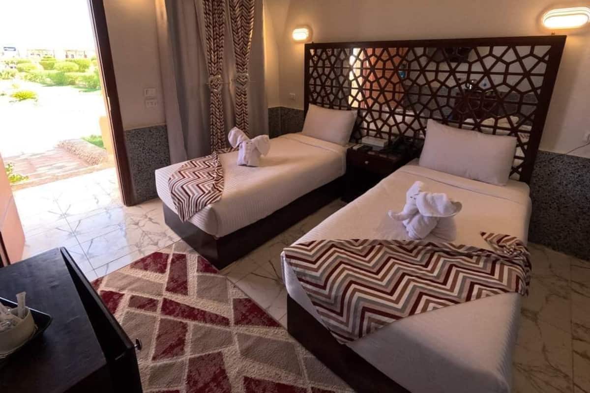 Habitación de hotel con dos camas, un cabecero estampado, un tapete rojo y blanco, y vistas a zonas verdes.