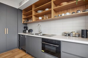 A modern kitchen with grey cabinets, a stainless steel sink, a built-in oven, and a wooden upper shelf with dishes.