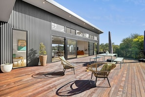 A modern house with a wooden deck, wicker furniture, and a large window overlooking the garden.