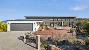 Une maison moderne avec un garage, un patio couvert avec des meubles d’extérieur et une vue sur l’océan.