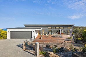 A modern house with a garage, a covered patio with outdoor furniture, and a view of the ocean. - Hakea Ridge Coastal Views 2 Decks Family Retreat (Fairhaven)