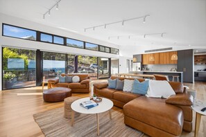 A spacious living area with a large brown leather sofa, a round coffee table, and a view of the outdoors through large glass doors.