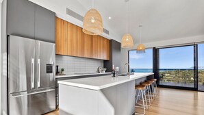 Une cuisine moderne dotée d’un grand îlot central, d’appareils électroménagers en acier inoxydable et offrant une vue sur la mer.