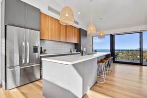 A modern kitchen with a large island, stainless steel appliances, and a view of the sea. - Hakea Ridge Coastal Views 2 Decks Family Retreat (Fairhaven)