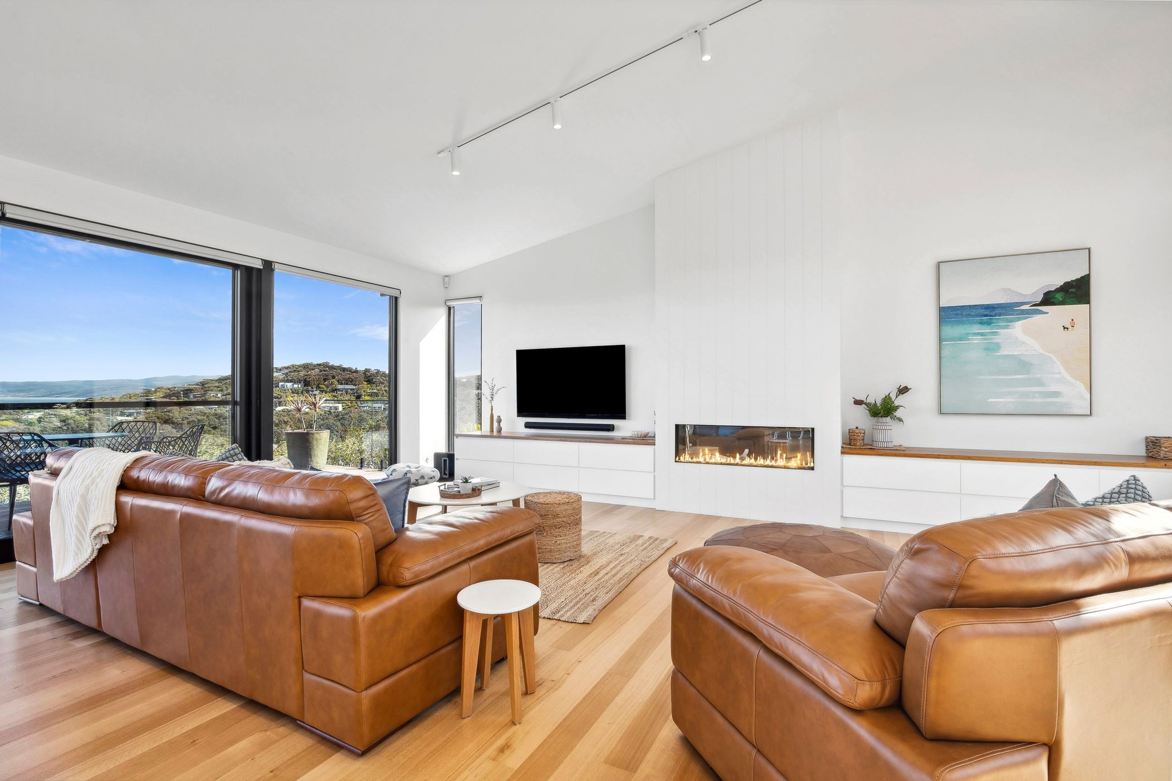 Un salon moderne avec des canapés en cuir, un téléviseur à écran plat, une cheminée et une grande fenêtre offrant une vue panoramique.
