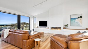 Un salon moderne avec des canapés en cuir, un téléviseur à écran plat, une cheminée et une grande fenêtre offrant une vue panoramique.