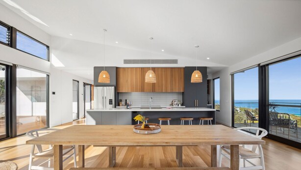 Une cuisine moderne avec des meubles en bois, des luminaires suspendus et une grande table à manger avec des chaises.