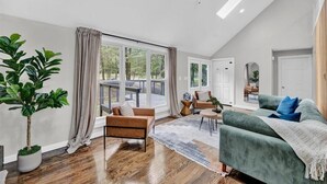 En rummelig stue med et stort vindue, en grøn sofa, en brun lænestol og en potteplante.