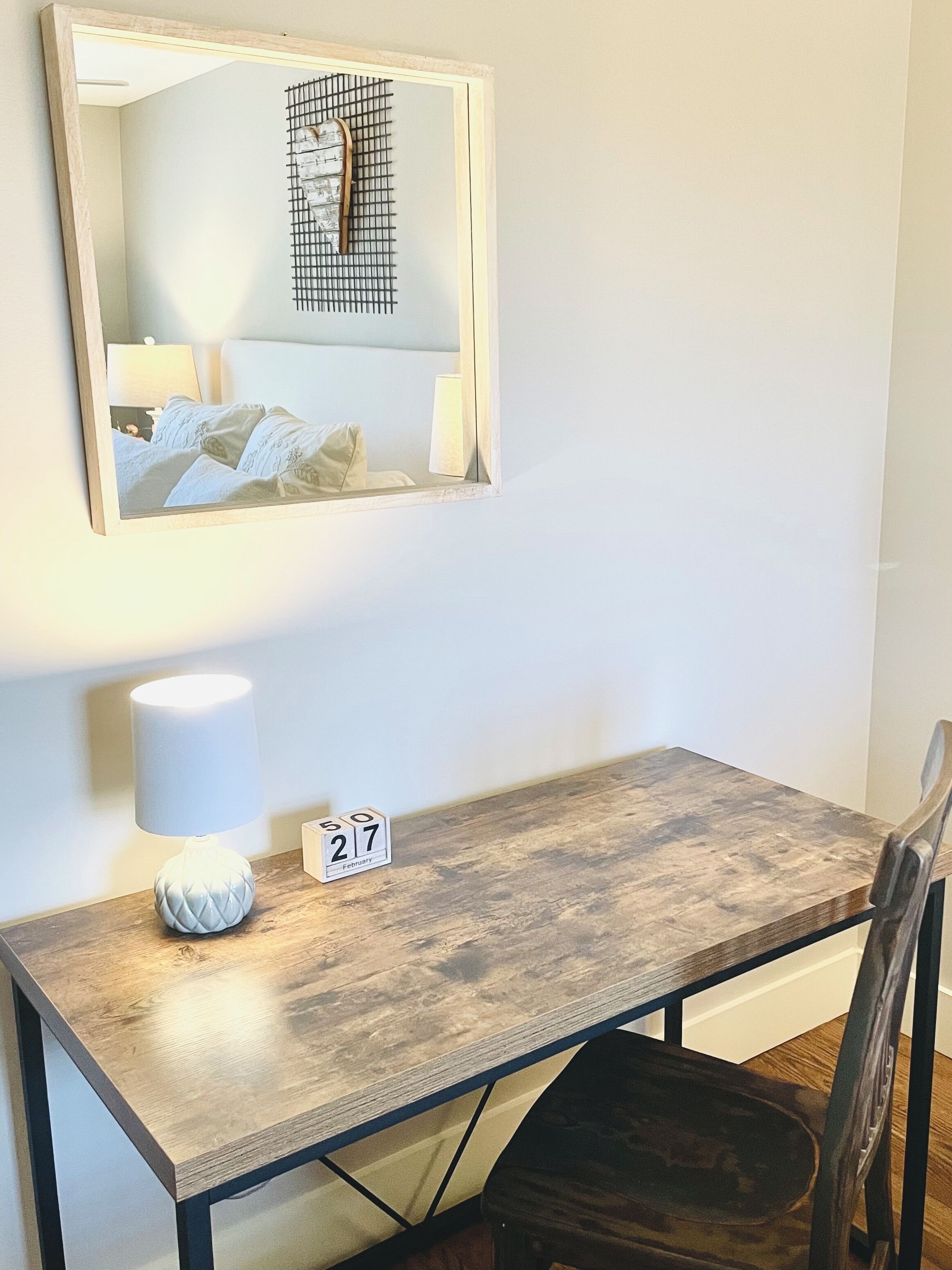 Une petite pièce, bien rangée, avec un bureau en bois, une chaise, une lampe et un miroir accroché au mur.