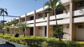 Un edificio de varios pisos con balcones, rodeado de follaje y palmeras.