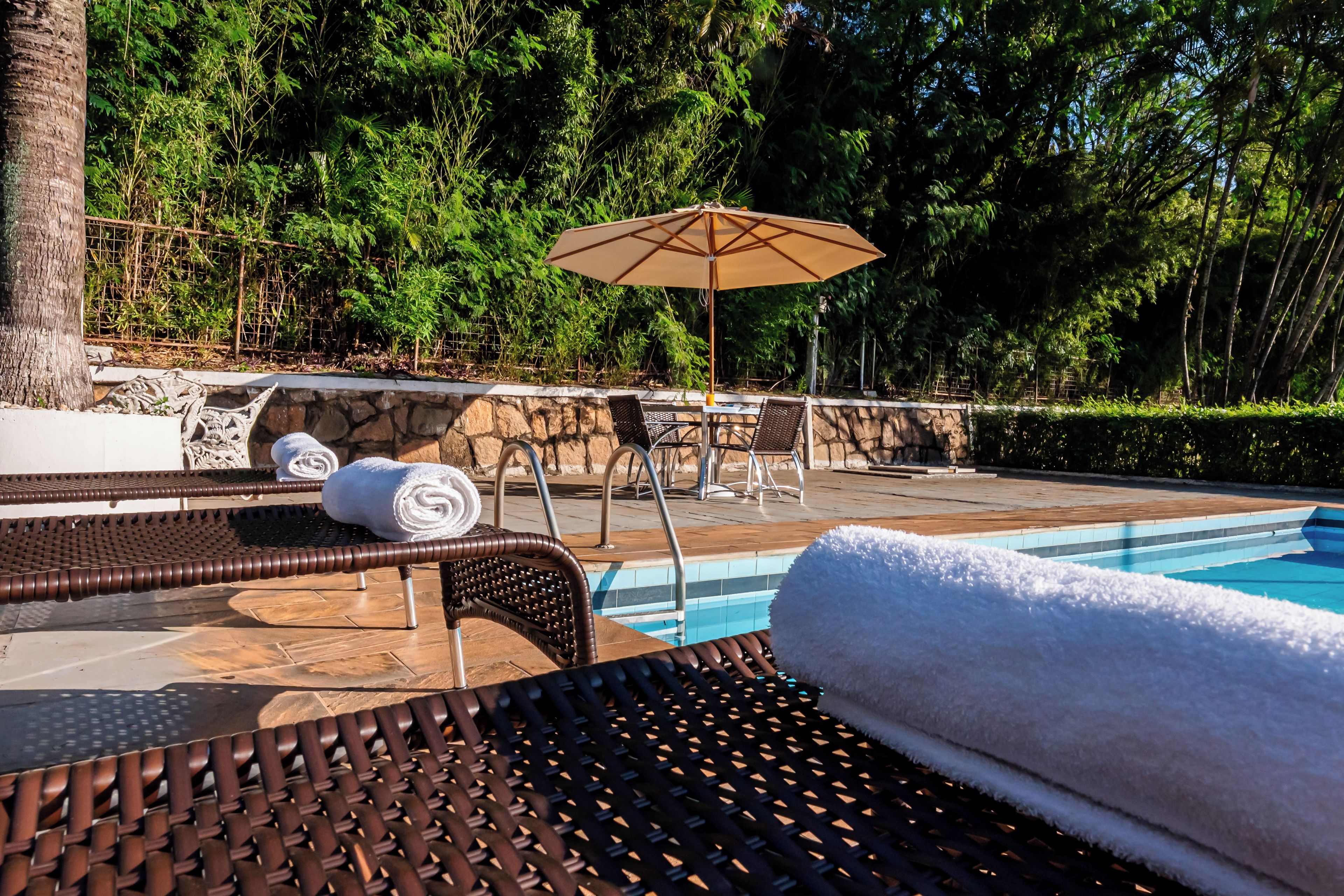 Un área junto a la piscina con sillas de descanso, una mesa y una sombrilla.