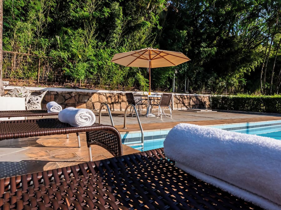Un área junto a la piscina con sillas de descanso, una mesa y una sombrilla.