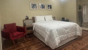Un dormitorio con una cama grande, una silla roja, una mesita de noche y tres cuadros en la pared.