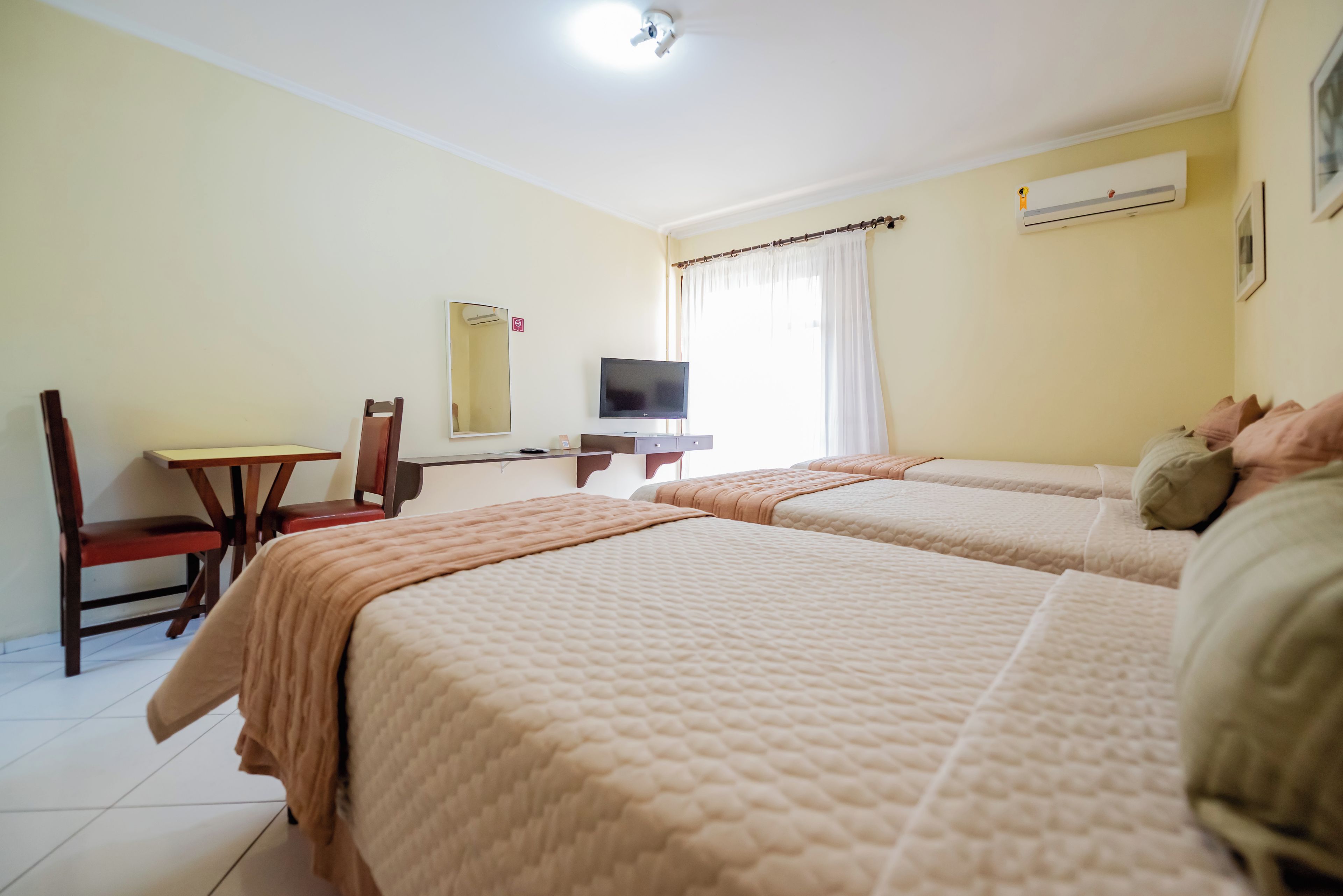 A hotel room with two beds, a desk, a chair, a television, and an air conditioning unit.