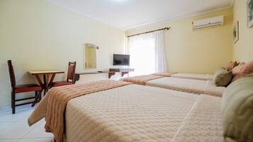 A hotel room with two beds, a desk, a chair, a television, and an air conditioning unit.