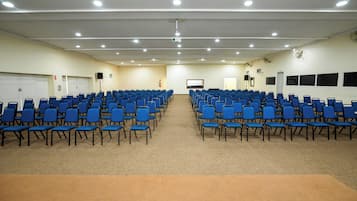 A conference room with rows of blue chairs, a carpeted floor, and a white ceiling with recessed lighting.