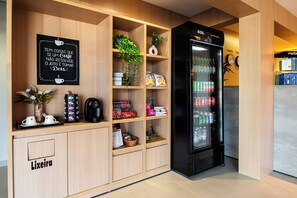 Un mini-bar d’hôtel comprenant une machine à café, des tasses à thé et à café, une plante, des en-cas et un réfrigérateur rempli de boissons.